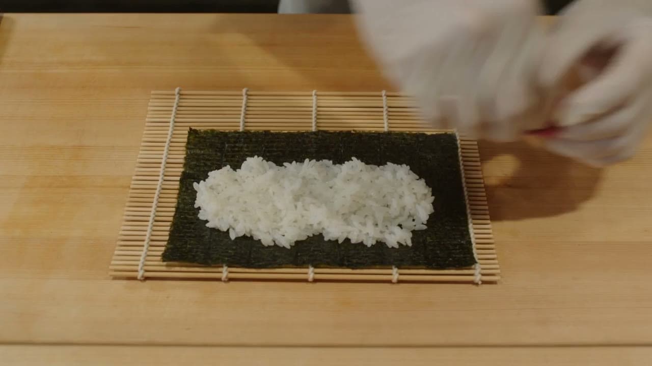 Hands spreading rice on nori over a bamboo mat